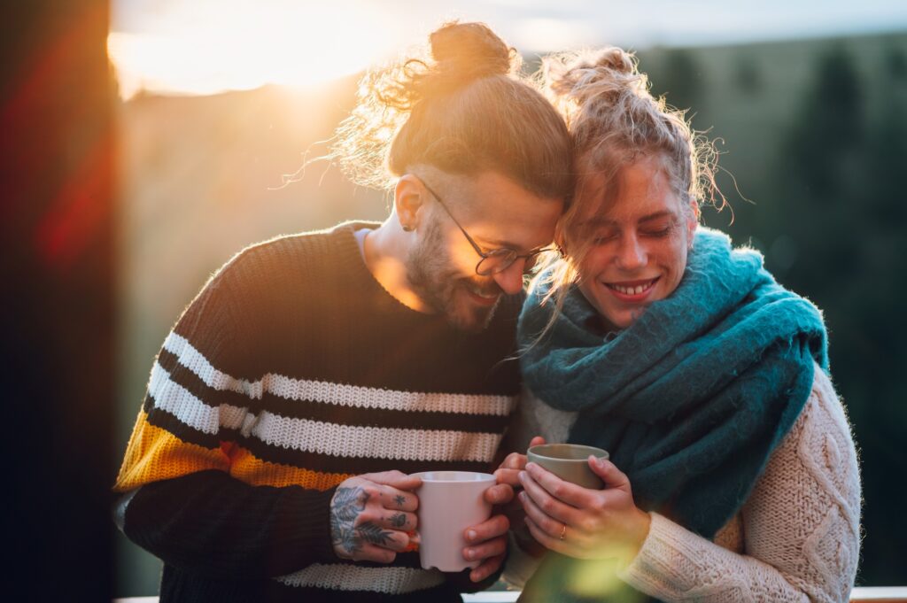 Young couple drinking coffee or tea while standing on their balcony at sunrise